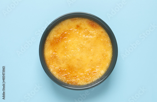 Delicious creme brulee in ceramic ramekin on light blue background, top view