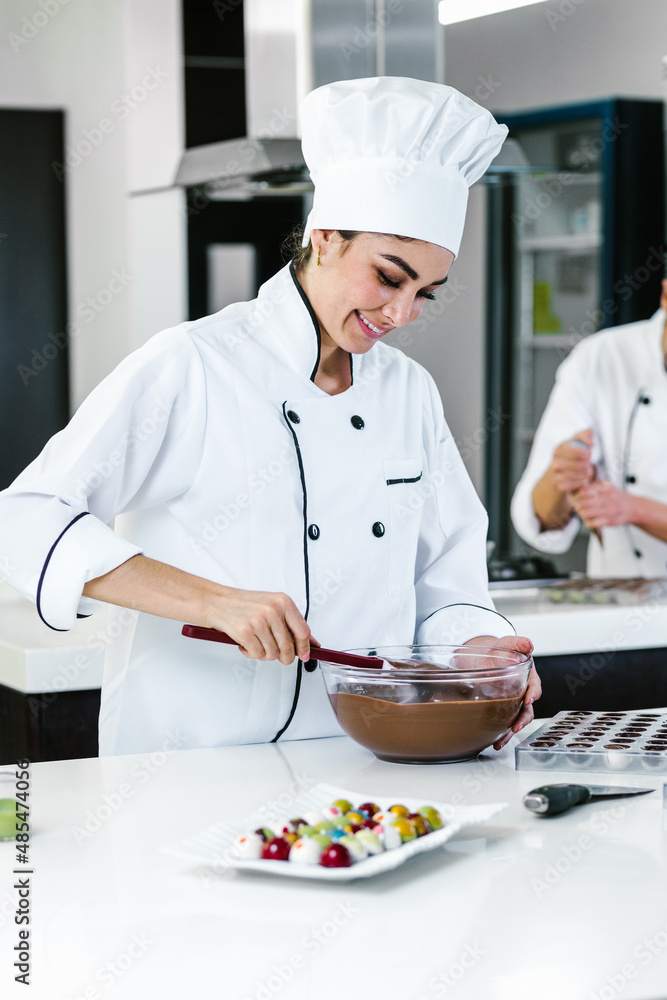 latin woman pastry chef wearing uniform holding a bowl preparing delicious sweets chocolates at kitchen in Mexico Latin America latin woman pastry chef wearing uniform holding a bowl preparing delicious sweets chocolates at kitchen in Mexico Latin America