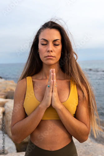 Vertical portrait of young caucasian woman meditating with hands in prayer by the sea.