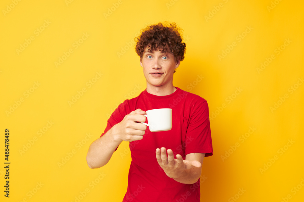 Young curly-haired man posing with a white mug and in the hands of a drink yellow background unaltered Young curly-haired man posing with a white mug and in the hands of a drink yellow background unaltered