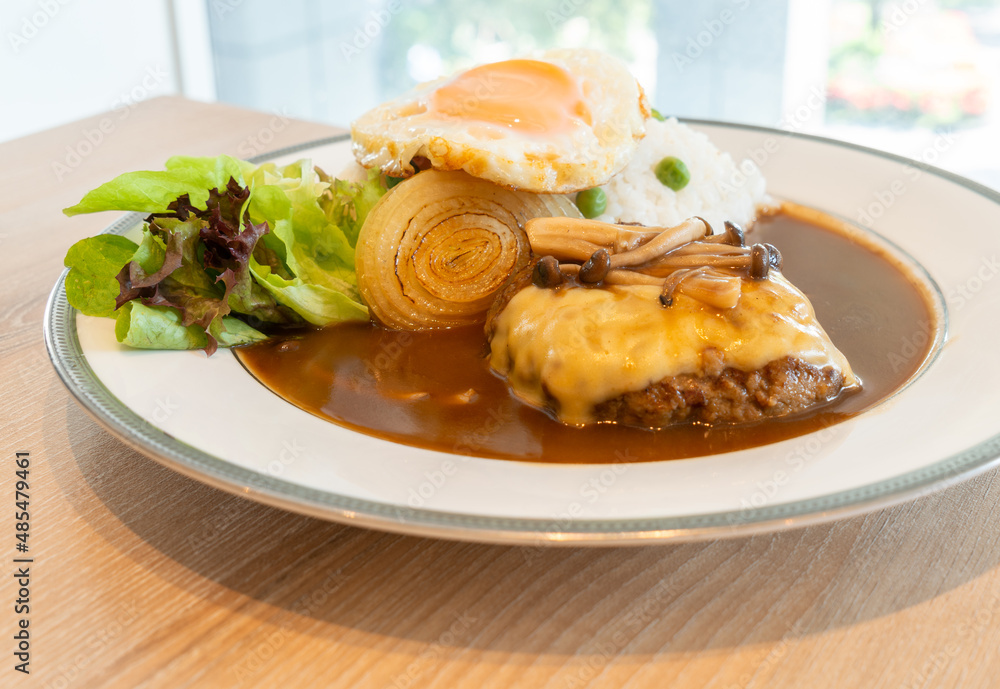 Close up Japanese Burger and curry with white rice, topped with cheese, Shimeji mushroom, fried egg. Food on a white round plate with fresh salad. Close up Japanese Burger and curry with white rice, topped with cheese, Shimeji mushroom, fried egg. Food on a white round plate with fresh salad.
