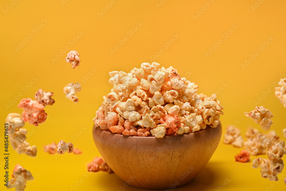 Flying popcorn from wooden bowl isolated on yellow background. Flying popcorn from wooden bowl isolated on yellow background.
