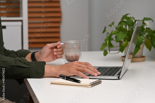 Businessman holding coffee cup and working with laptop computer home office.