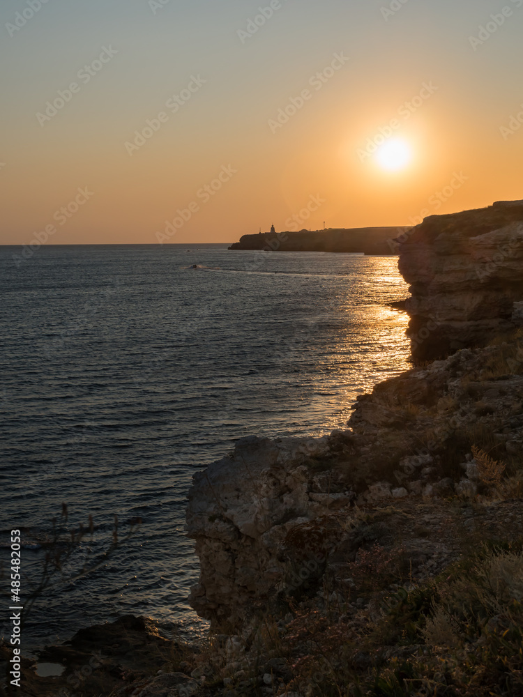Sunset on the sea. View from the cliff. Path from the outgoing sun rays to the sea. Orange sky. Steep rocks. Vertically. Copy space