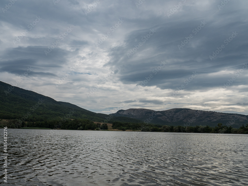 
Clouds over a mountain lake. Green forested mountains in the background. Pure natural water. Horizontally