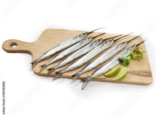 Fresh Ballyhoo halfbeak or Ballyhoo Fish (Hemiramphus brasiliensis) is decorated with herbs and vegetables on a wooden pad.Selective Focus. photo