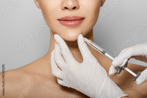 Syringe near woman's chin, beauty injections with fillers for chin shape correction. Cropped female face while procedure chin contouring photo