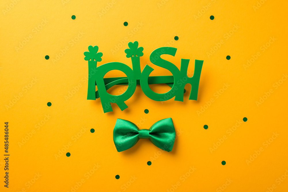 Top view photo of st patrick's day decorations funny outfit irish party glasses and green bow-tie on isolated yellow background Top view photo of st patrick's day decorations funny outfit irish party glasses and green bow-tie on isolated yellow background