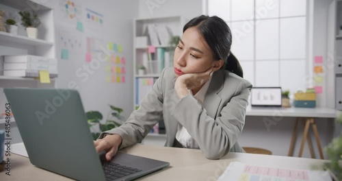 Young Asian businesswoman sit on desk with laptop overworked tired burnout syndrome at office. Exhausted lady with sleeply eye at workplace, Girl not enjoy unhappy with work, Work mental health. photo