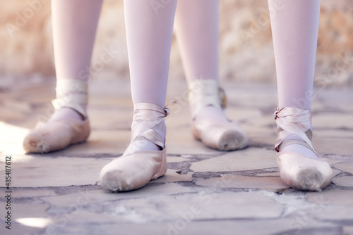 Feet of two ballerinas standing in a row on a stone floor at an outdoor rehearsal