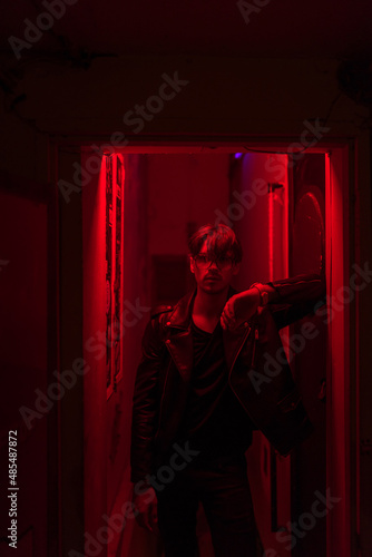 Portrait of young stylish brunet caucasian man in black leather jacket standing in red neon light. High quality photo