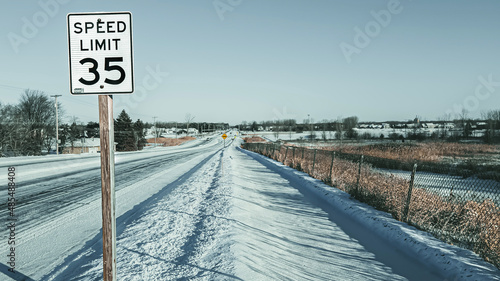 Speed limit sign and winter landscape with snow covered road and sidewalk