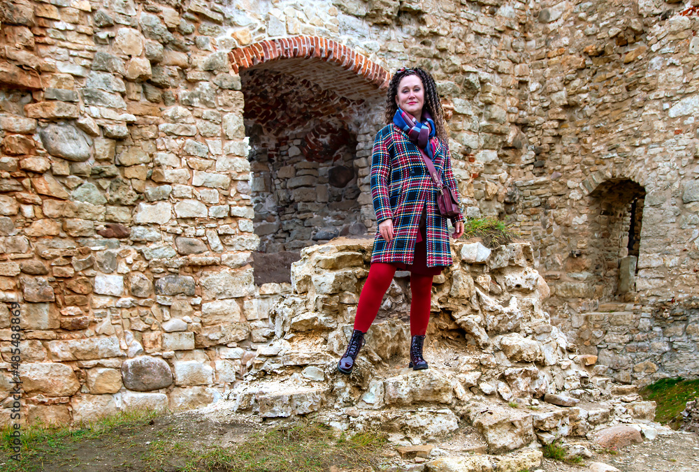 Pretty woman with curly hair stands on the ruins of an medieval castle remains in Koknese, Latvia. Built shortly after 1209.