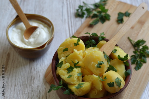 Coocked potatoes in brown clay bowl and suare cream in small one, decorated with parsley on kitchen table photo