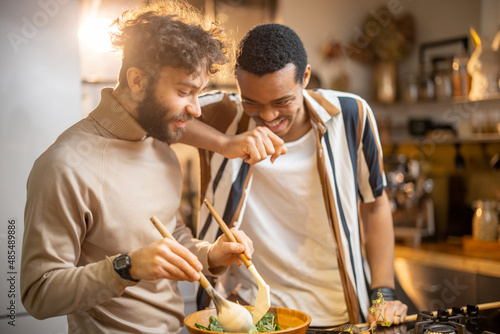 Fotografie Two guys of different ethnicity having fun while making salad together on kitchen