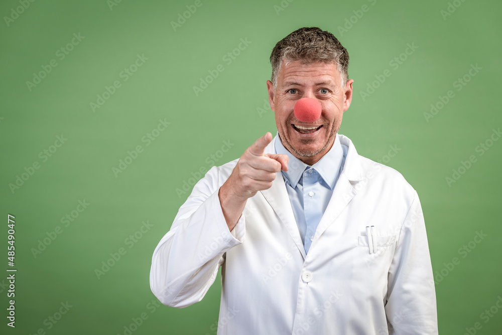 Scientist with white coat has red clown nose on and stands in front of green background Scientist with white coat has red clown nose on and stands in front of green background