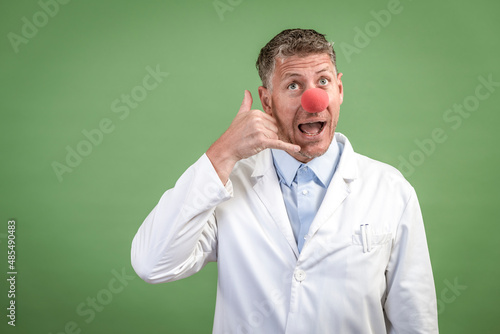 Scientist with white coat has red clown nose on and stands in front of green background