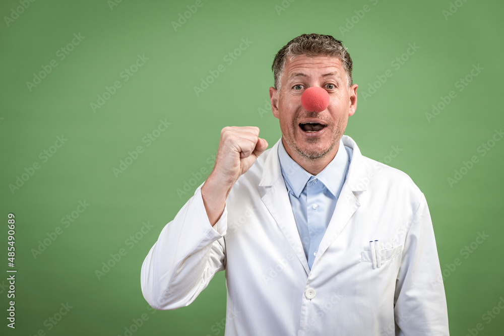 Scientist with white coat has red clown nose on and stands in front of green background Scientist with white coat has red clown nose on and stands in front of green background