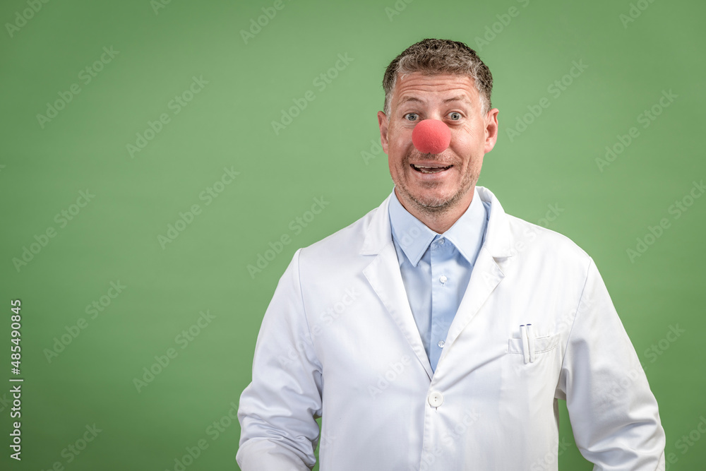 Scientist with white coat has red clown nose on and stands in front of green background