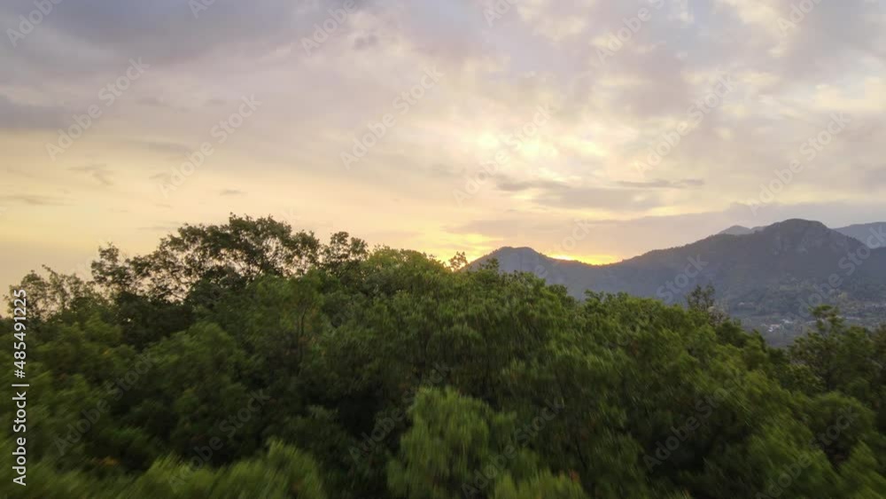 Beautiful aerial forwarding shot of sunrise over a scenic mountain range with the view of a small town at the foothills of the range with lush green vegetation in Montenegro. Beautiful aerial forwarding shot of sunrise over a scenic mountain range with the view of a small town at the foothills of the range with lush green vegetation in Montenegro.