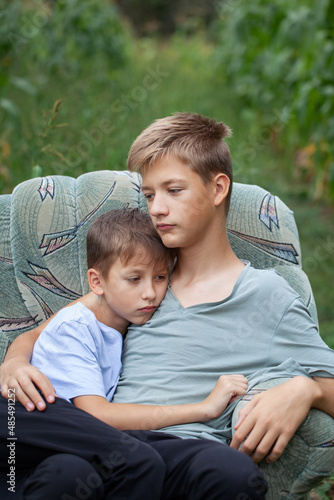 Two serious brothers sitting on a armchair in a field in the countryside in summer day.