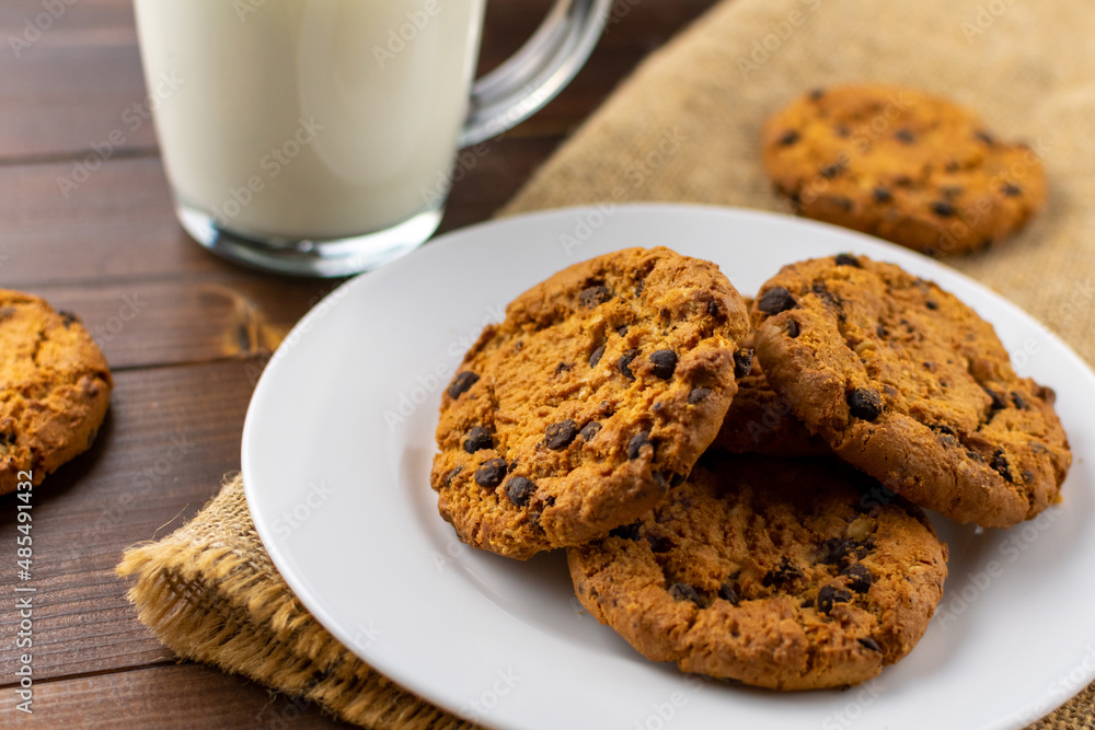 A bunch of delicious chocolate chip cookies on a white plate with a cup of milk. Close Up. A bunch of delicious chocolate chip cookies on a white plate with a cup of milk. Close Up.