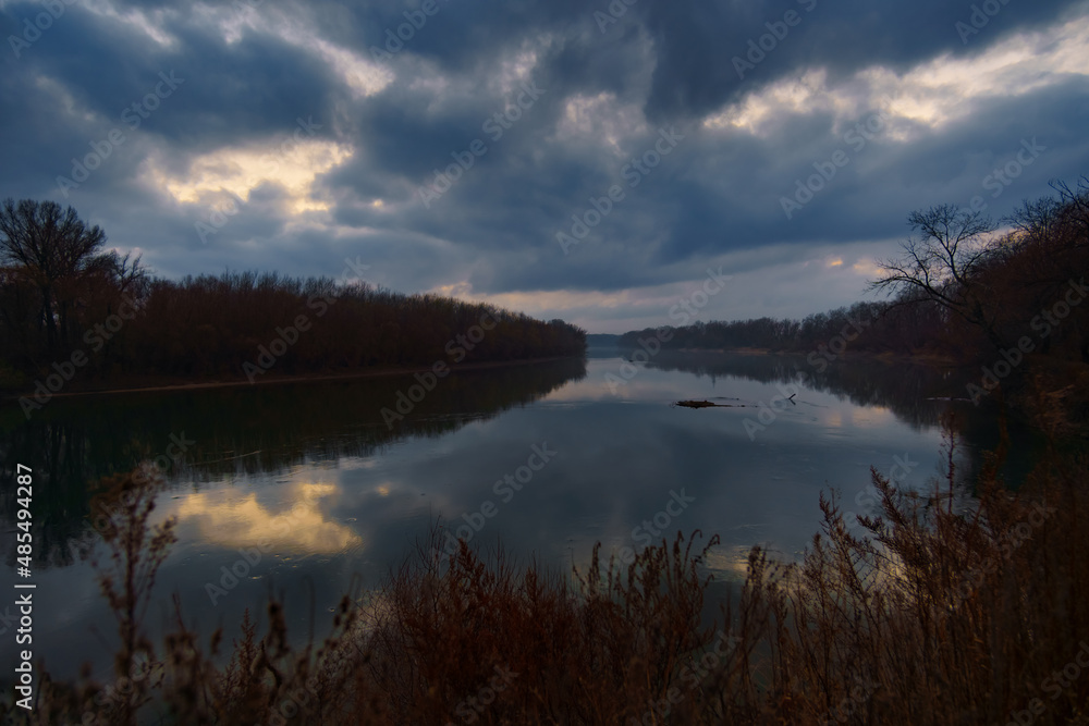 a beautiful autumn landscape in the evening - forest with river and cloudy sky