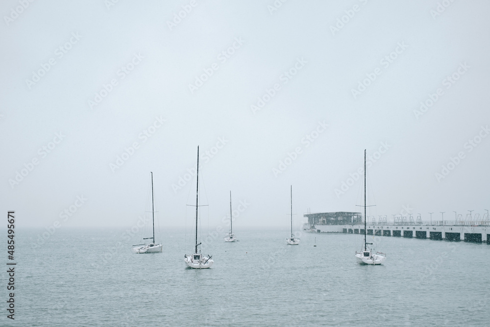 Several sailing yachts are moored at the pier in the sea. Cold weather in winter season and snowfall. Several sailing yachts are moored at the pier in the sea. Cold weather in winter season and snowfall.