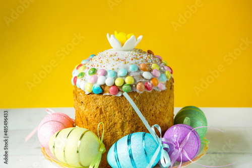 Easter cake with painted eggs on a platter in a white table. Traditional festive food. Yellow background photo