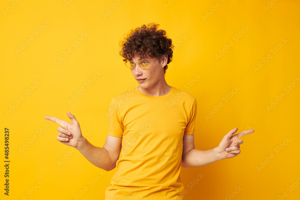 Young curly-haired man wearing stylish glasses yellow t-shirt posing isolated background unaltered Young curly-haired man wearing stylish glasses yellow t-shirt posing isolated background unaltered