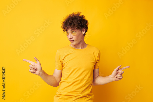 Young curly-haired man wearing stylish glasses yellow t-shirt posing isolated background unaltered