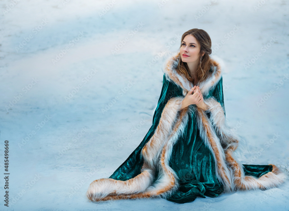 Fantasy woman sits on white snow in winter forest. Princess girl smiling  face. Green long velvet