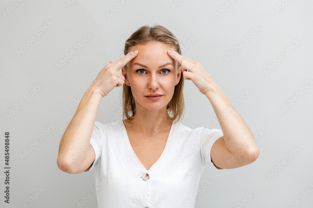 Portrait of a young beautiful woman, pulling the skin on her forehead with her fingers. Gray background. The concept of rejuvenation and facial wrinkles Portrait of a young beautiful woman, pulling the skin on her forehead with her fingers. Gray background. The concept of rejuvenation and facial wrinkles