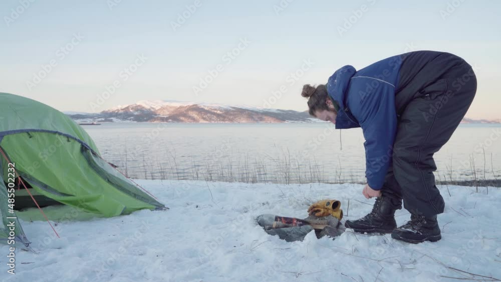 Man Tying His Boots Near Campfire In Front Of His Tent At Wintertime. - static Man Tying His Boots Near Campfire In Front Of His Tent At Wintertime. - static