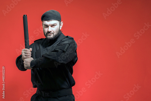 Mercenary. Defender. A male guard in a black uniform and a cap took up a defensive position, holding a baton with both hands. Bodyguard. Private security