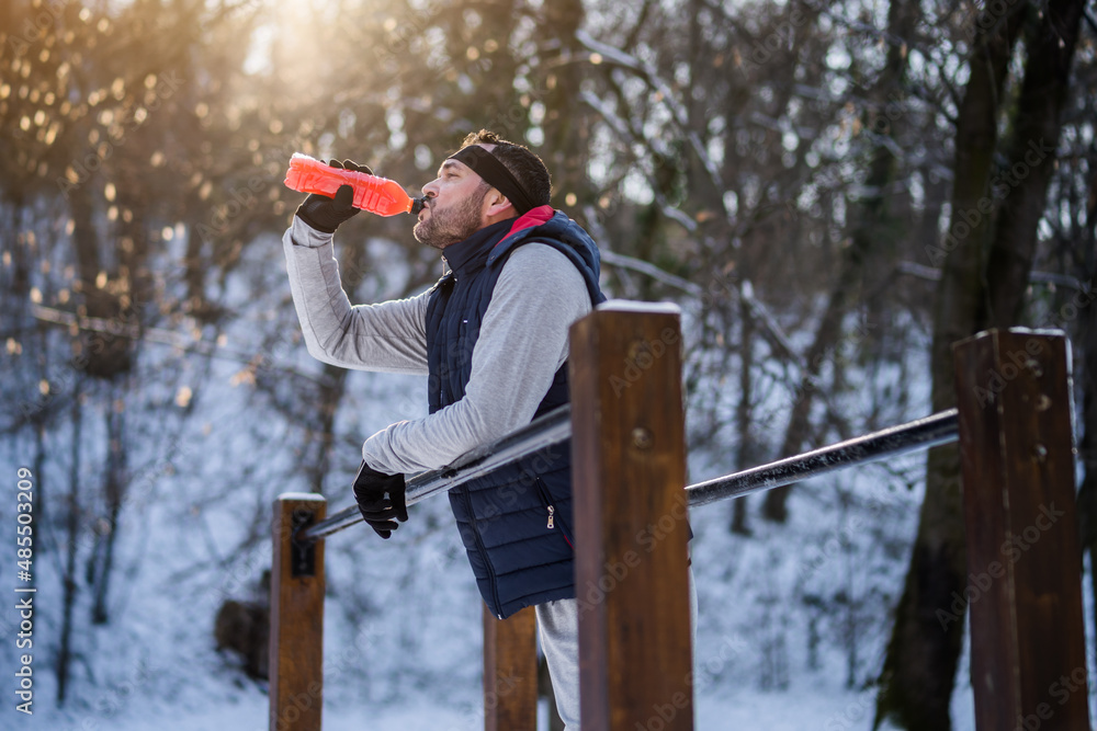 Adult man is ready for exercising on push-up bar in park in wintertime. He is drinking hydration boost juice. Adult man is ready for exercising on push-up bar in park in wintertime. He is drinking hydration boost juice.