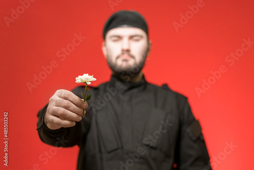 The bodyguard gives a succulent. A male guard in black uniform and a cap holds a flower forward. Handsome brutal man. Military. Defender of the law and order. Mercenary