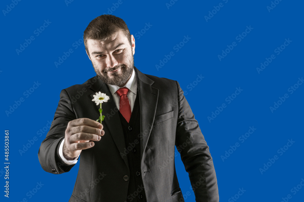 A smiling man in a business suit with a red tie gives a chamomile flower. Sexy male look. Brutal person. Romantic. Women's holiday. International women's day. A smiling man in a business suit with a red tie gives a chamomile flower. Sexy male look. Brutal person. Romantic. Women's holiday. International women's day.
