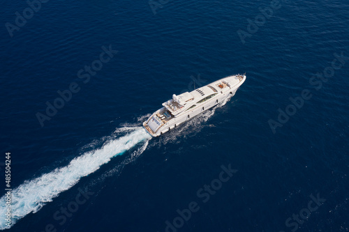 Big white super boat moves in the ocean aerial view. Big yacht for millionaires in the sea drone view. Luxury white mega yacht fast moving on dark water making a trail in the ocean top view. © Berg