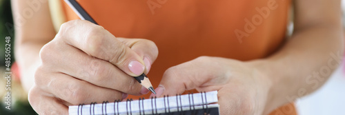 Female waiter writing down ordered dishes in notebook with pencil closeup