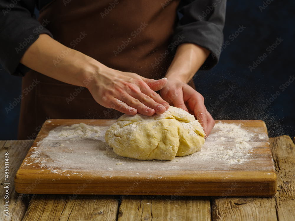 Dough on a wooden cutting board, prepared by the hands of the chef. Close-up. Dark background. Minimalism. preparation of dough products - bread, pizza, pie, pasta, ravioli.