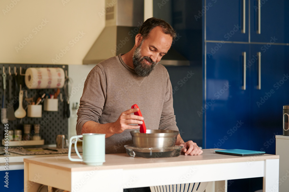 Portrait of a smiling middle-aged bearded man checking the temperature of bread dough early in the morning at home Portrait of a smiling middle-aged bearded man checking the temperature of bread dough early in the morning at home