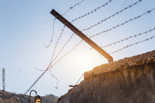 Close-up view prison or border concrete wethered fence broken old rusty barbed wire chain security barrier silhouette sky sun background. Dictatorship tyranny repression regime end freedom concept photo