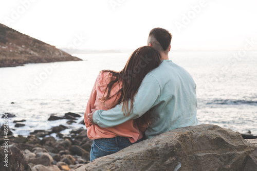 Young caucasian woman and man embracing each other at a rocky beach while sunset. photo