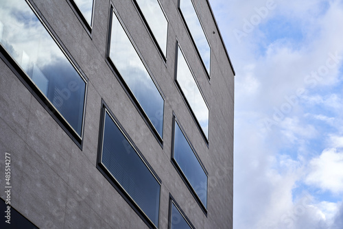 Modern building facade of residential and commercial premises. Rectangular large windows in gray house. Blue cloudy sky. Up view.