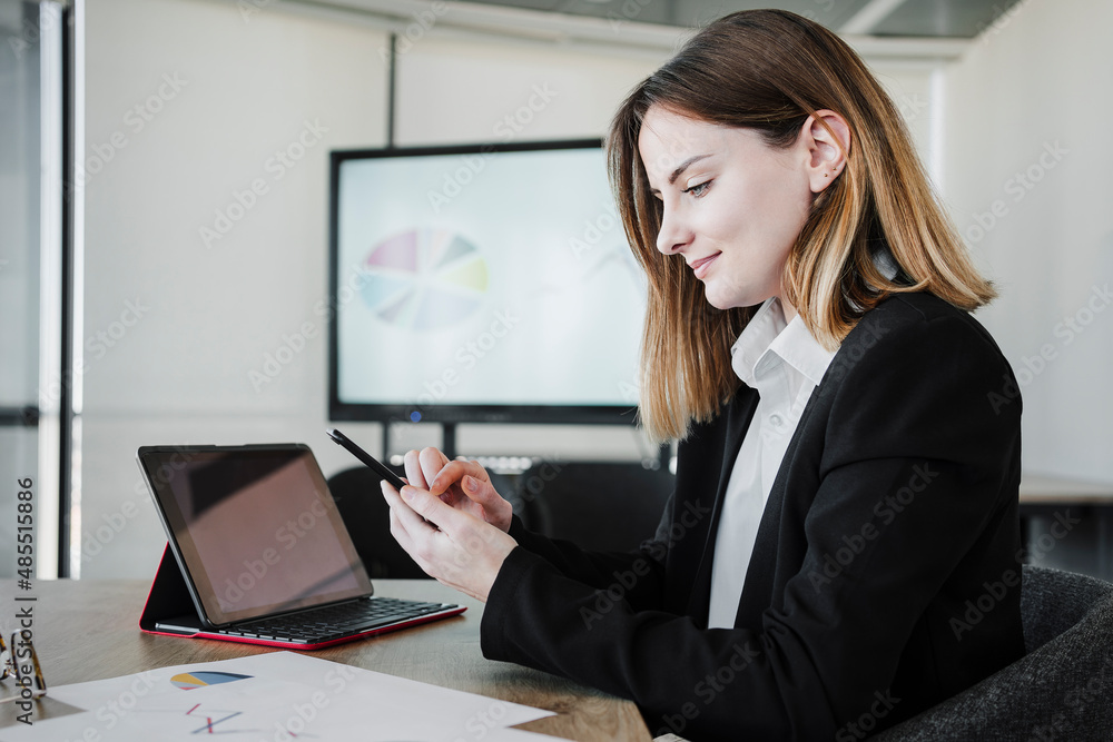 Smiling businesswoman using smart phone by tablet PC in office Smiling businesswoman using smart phone by tablet PC in office
