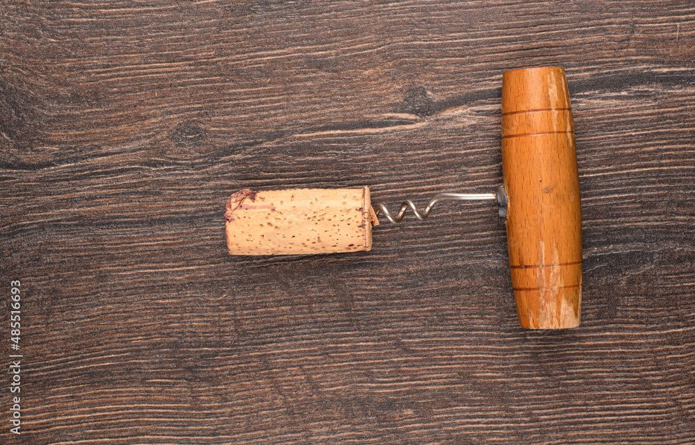 Top view of a wine cork with a corkscrew on a wooden background.