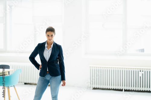 Confident businesswoman with hand on hip standing at office photo