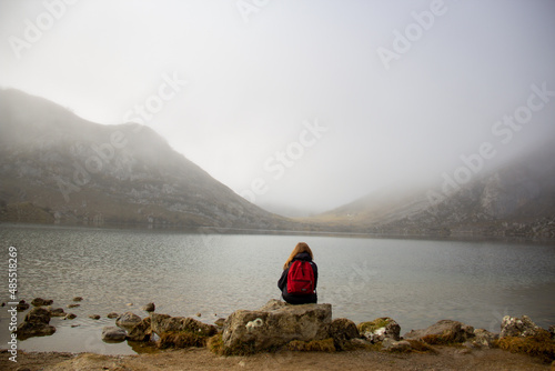 Mujer rubia encuadrada en un placido paisaje nublado en un lago, a los pies de unos pequeños montes photo