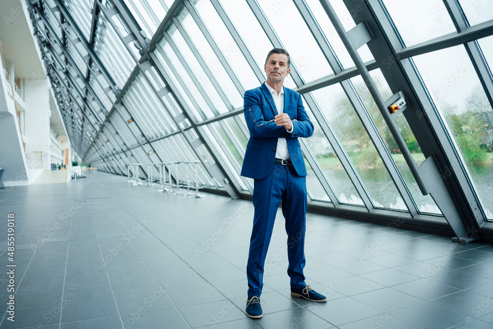 Businessman holding eyeglasses standing at office Businessman holding eyeglasses standing at office